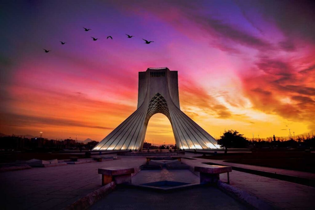 A flock of birds soaring over a tall building against the backdrop of a vibrant sunset